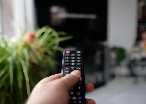 Man is holding a TV remote while selecting a program on the flat screen TV in Stock Photos