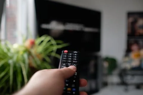 Man is holding a TV remote while selecting a program on the flat screen TV in Stock Photos
