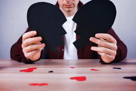Man holding two halves of a broken black paper heart. Concept of heartbreak.. Stock Photos