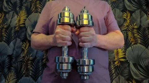 Man holding two metallic dumbbells in a symmetrical pose against a patterne.. Stock Photos
