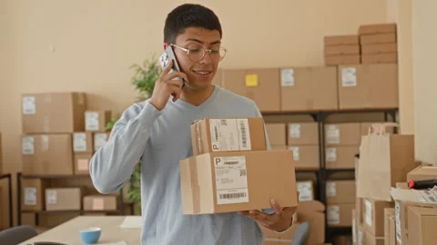 Man holding two shipping boxes and phone to ear, talking while packing shel.. Stock Footage 339252791