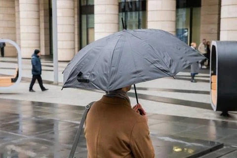 Man holding umbrella while walking on city street during rain. Back view of.. Fotos Stock