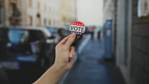 Man holding vote button on street showcasing election engagement outdoors w.. Stock Footage 311523746