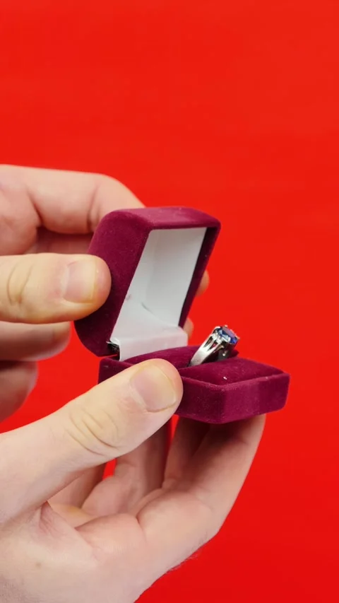 Man holding wedding ring in box for proposal on red background. Vertical video Stock Footage 325331803