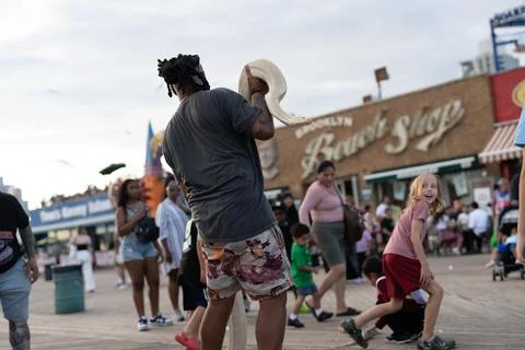 Man holding a white snake on a crowded boardwalk Photos