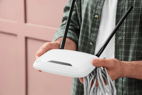 Man holding a white wireless router with antennas and network cables, interne Stock Photos