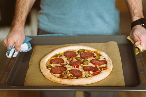 A man holds a baking sheet with pizza. Baking sheet covered with baking paper Stock Photos