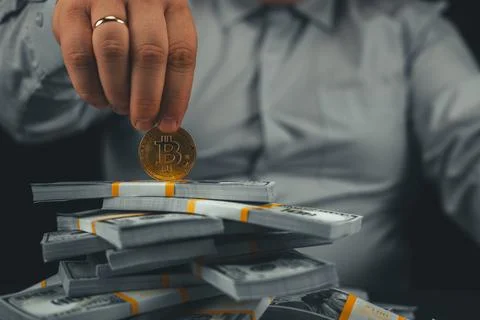 A man holds a bitcoin coin on a stack of stacks of dollars on a black background Stock Photos