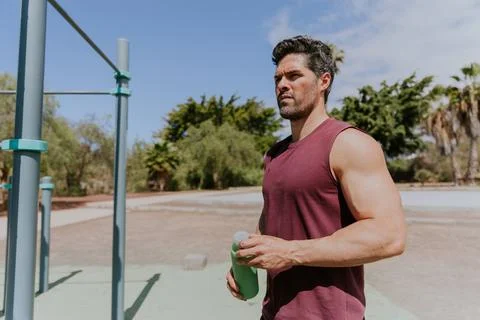 A man holds a bottle of water while training outdoors, hydration concept Stock Photos