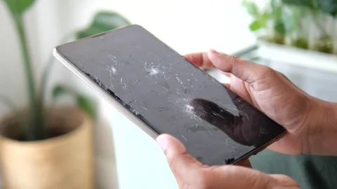 Man holds a broken tablet with cracks on the screen in a bright room Stock Footage 346578581