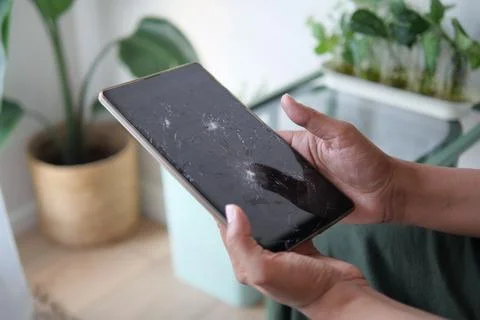 Man holds a broken tablet while sitting near plants in a bright room Stock Photos