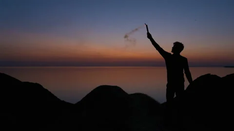 The man holds a burning fire stick on the seascape background. slow motion 動画素材 143570930