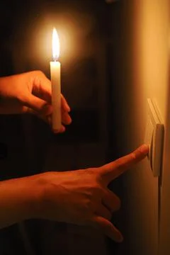 A man holds a candle while reaching for a light switch in a dark room. Stock Photos