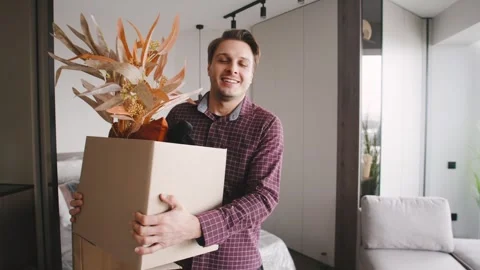 A man holds a cardboard box filled with plants and decorative items. Boxes are Stock Footage 346229648