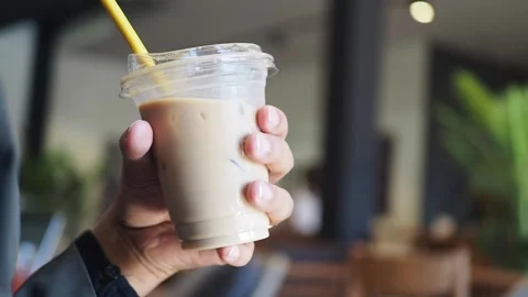 Man holds cold coffee drink at cafe table during daytime in a modern setting Stock Footage 346738521