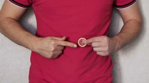 A man holds a condom in his hand, shows OK with the other hand. The concept of s Stock Footage 235707992