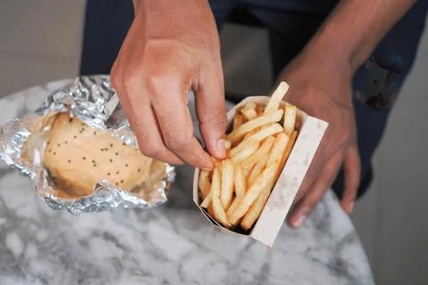 Man holds a container of fries while sitting at a table with food Stock Photos