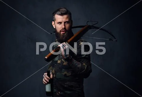 A man holds the craft beer bottle and a crossbow. Stock Photos