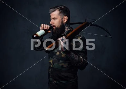 A man holds the craft beer bottle and a crossbow. Stock Photos