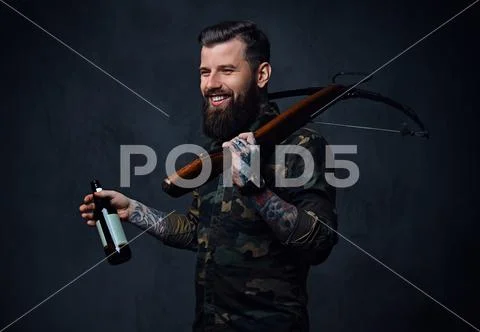 A man holds the craft beer bottle and a crossbow. Stock Photos