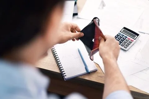Man holds an empty wallet over a desk with bills and a calculator, struggli.. Stock Photos