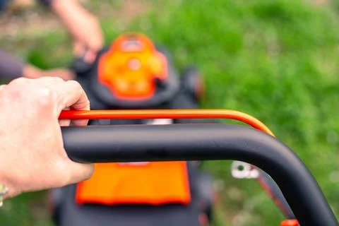 A man holds the engine speed control lever of a petrol lawn mower with his .. Foto stock