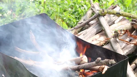 A man holds fire on the grill. Adds firewood to the fire. Nearby are firewood Stock Footage 134974343