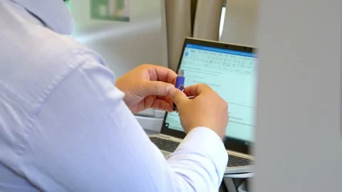 A man holds a flash drive in his hands while working on a laptop during Stock Footage 204876701