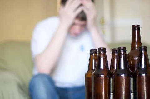 Man holds head with group of empty beer bottles Stock Photos