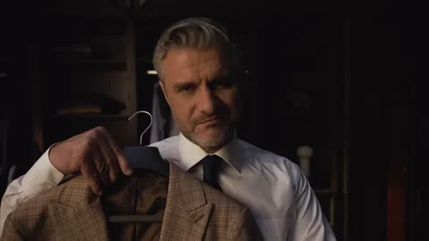 Man holds a jacket on a hanger and tries it on himself, chooses jacket to wear Video stock 235353281