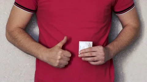 A man holds a packaged condom in his hand, with the other hand he shows OK. The Stock Footage 236028273