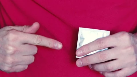 A man holds a packed condom in his hand, shows OK with the other hand. The conce Stock Footage 235708111