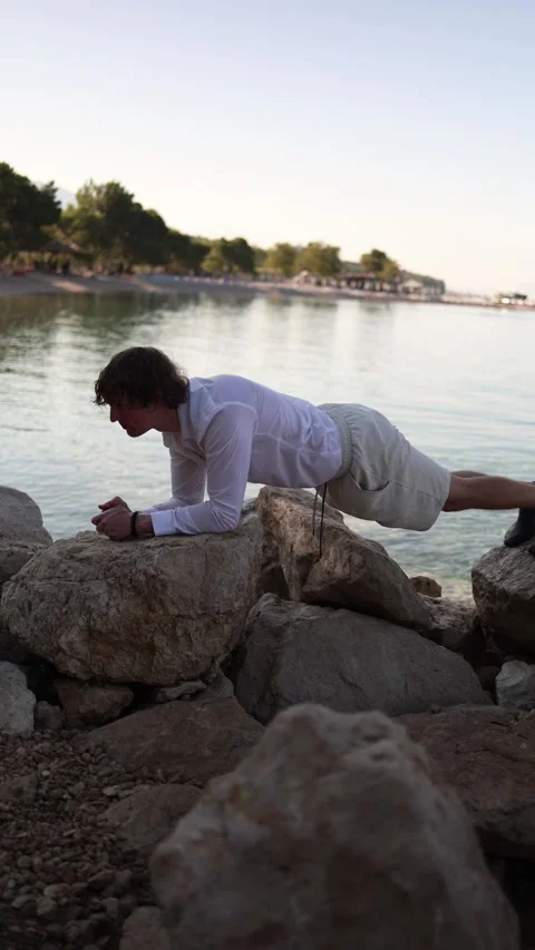 Man holds a plank on seaside rocks refusing to pause his workout routine on vaca Stock Footage 341621812