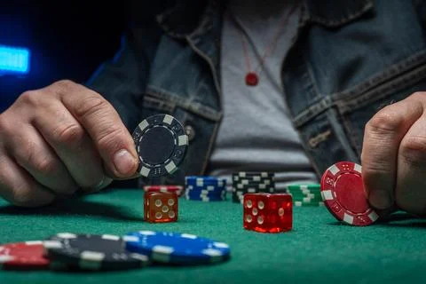A man holds a poker chip while sitting at a green table covered with variou.. Foto stock