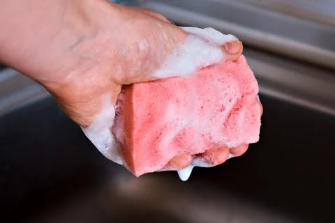 A man holds a red kitchen sponge in his hand, which is foamed from detergent, Stock Photos