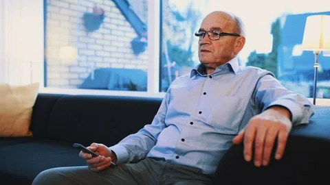 Man holds on to remote control as he watches television in his living room Stock Footage 99012905