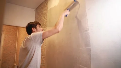 A man holds a roller in his hands and covers the putty wall with glue Vidéo 146041438