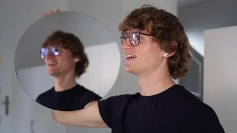 Man holds a round mirror smiling at his reflection with cheerful curiosity as if Stock Footage 312981816