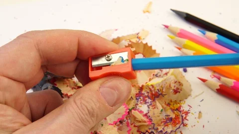 A man holds a sharpener in his hands and sharpens colored pencils. Stock Footage 125549785