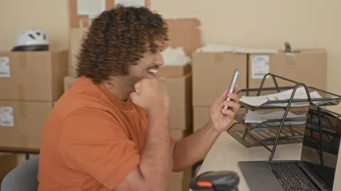 Man holds smartphone and pumps fist at desk amid cardboard boxes in buildin.. Stock Footage 337402602