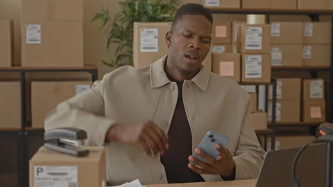 Man holds smartphone in hand while checking parcels and raising arm beside .. Stockbeeldmateriaal 337434798