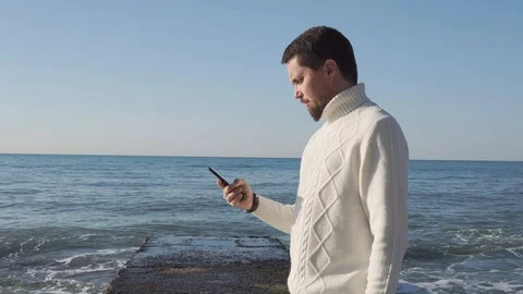 Man holds a smartphone in his hands, the person stands on a background of waves Stock Footage 88563946