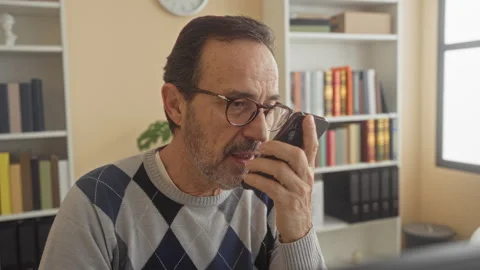 Man holds smartphone to mouth while speaking near desk and computer in a bu.. Stock Footage 337442370