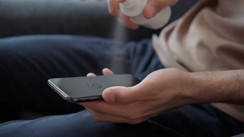 Man holds smartphone, sprinkles the solution, wipes it with a napkin Stock-Footage 127345271