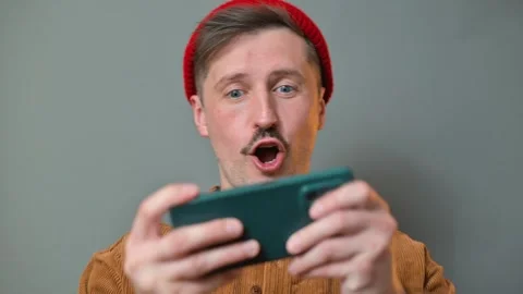 A man holds a smartphone while playing a game. He shows different expressions Stock Footage 337643184