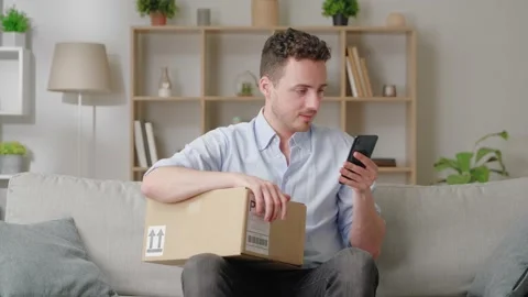 Man holds smartphone while sit on sofa with box, using parcel tracking Stock Footage 169017372
