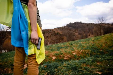 A man holds a weapon in his hand against the background of the Ukrainian flag. Stock Photos