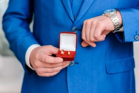 A man holds wedding rings in a red box in his hands and looks at his watch Stock Photos