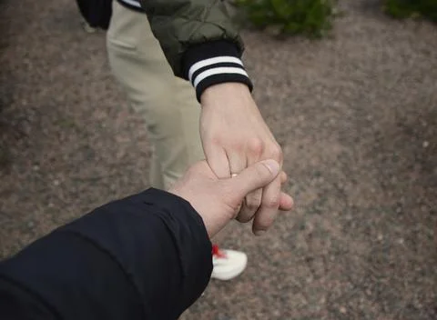 A man holds a woman's hand while walking outdoors Stock Photos