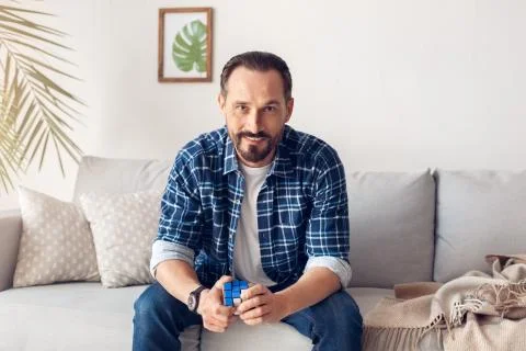 Man home alone sitting on sofa with rubik's cube looking camera cheerful Stock Photos